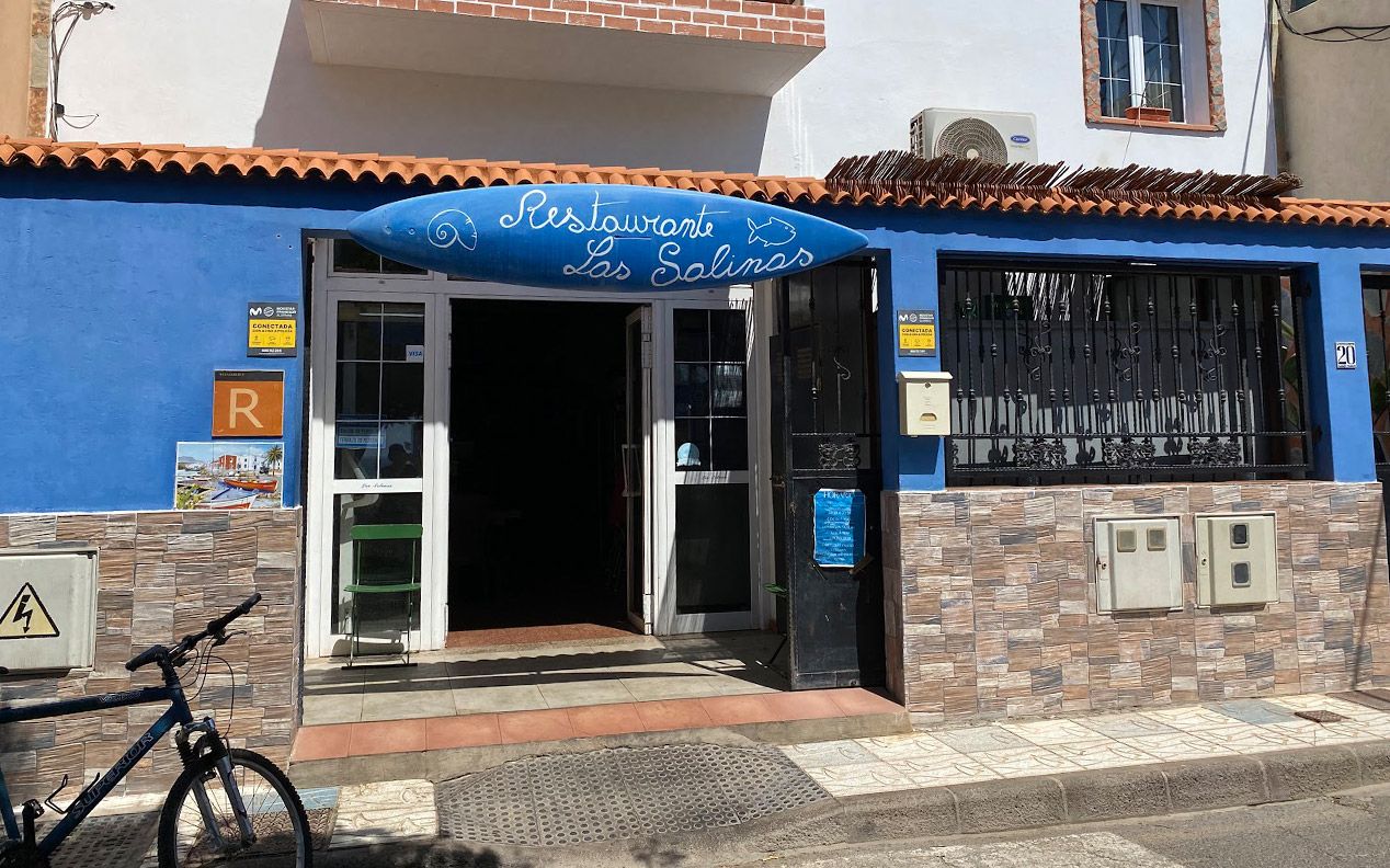 Fachada azul del Restaurante Las Salinas con el cartel pintado a mano sobre una tabla de surf